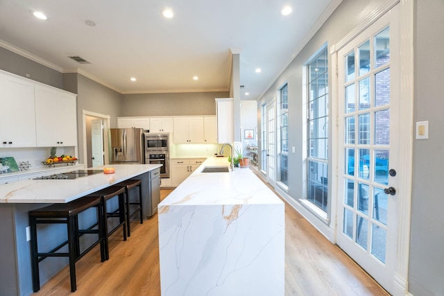 kitchen with a center island, sink, stainless steel appliances, white cabinets, and light stone counters