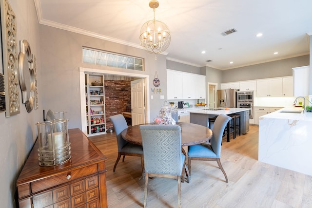 dining room featuring an inviting chandelier, crown molding, light hardwood / wood-style floors, and sink