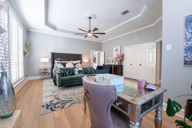 bedroom featuring a closet, ornamental molding, light wood-type flooring, ceiling fan, and a tray ceiling