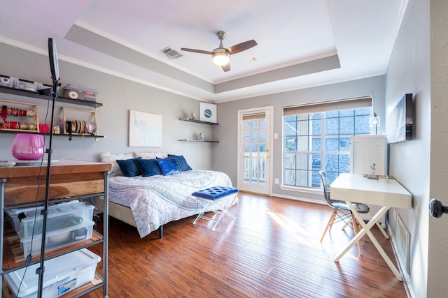 bedroom featuring ceiling fan, a raised ceiling, access to exterior, wood-type flooring, and ornamental molding