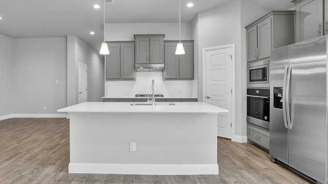 kitchen with decorative light fixtures, stainless steel appliances, light hardwood / wood-style floors, a kitchen island with sink, and gray cabinetry