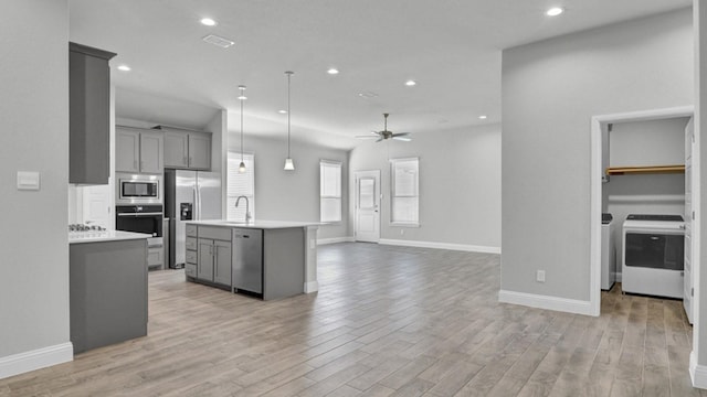 kitchen with pendant lighting, appliances with stainless steel finishes, a kitchen island with sink, ceiling fan, and gray cabinetry