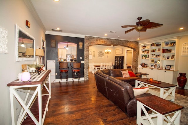 living room featuring ceiling fan with notable chandelier, dark wood-type flooring, brick wall, and ornamental molding