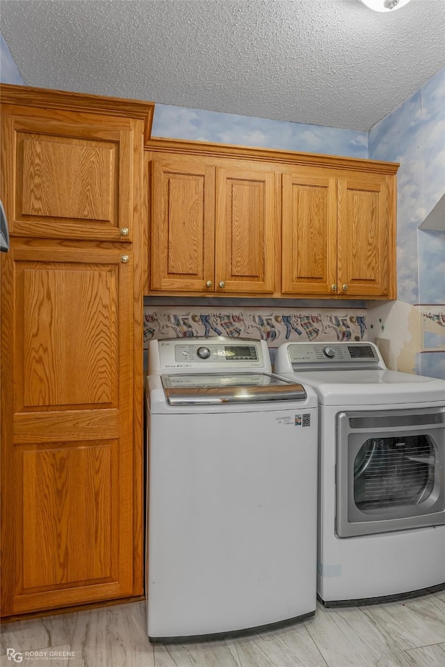 clothes washing area with a textured ceiling, cabinets, and washing machine and dryer