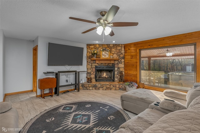 living room featuring ceiling fan, a fireplace, wooden walls, and a textured ceiling