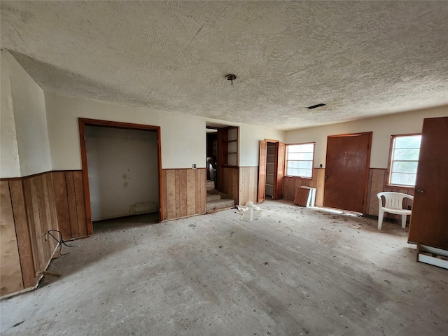 interior space with wood walls, a textured ceiling, and wainscoting