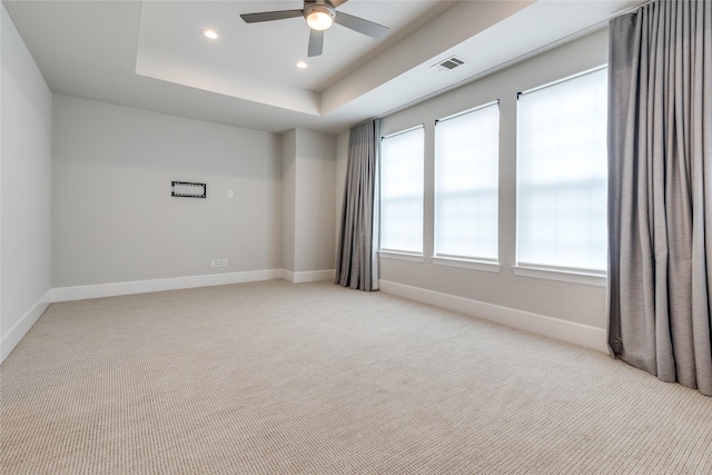 empty room featuring light carpet, ceiling fan, and a tray ceiling