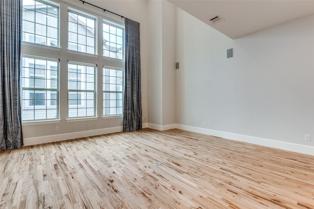 spare room featuring light hardwood / wood-style floors and a towering ceiling