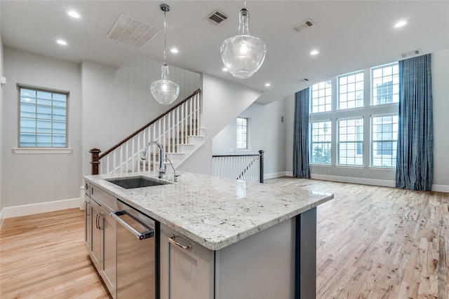 kitchen featuring pendant lighting, dishwasher, sink, light stone counters, and a center island with sink