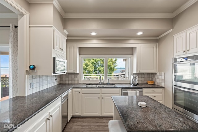 kitchen featuring appliances with stainless steel finishes, white cabinetry, dark stone counters, sink, and backsplash