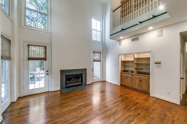 unfurnished living room featuring dark wood-type flooring, plenty of natural light, a fireplace, and a high ceiling