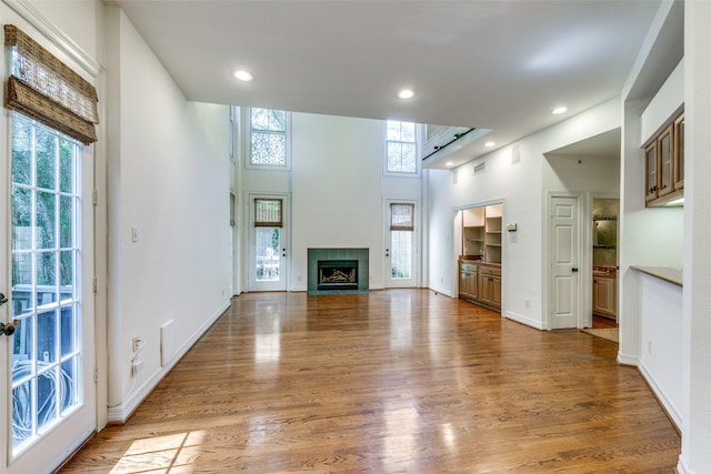 unfurnished living room featuring a towering ceiling, a fireplace, and wood-type flooring