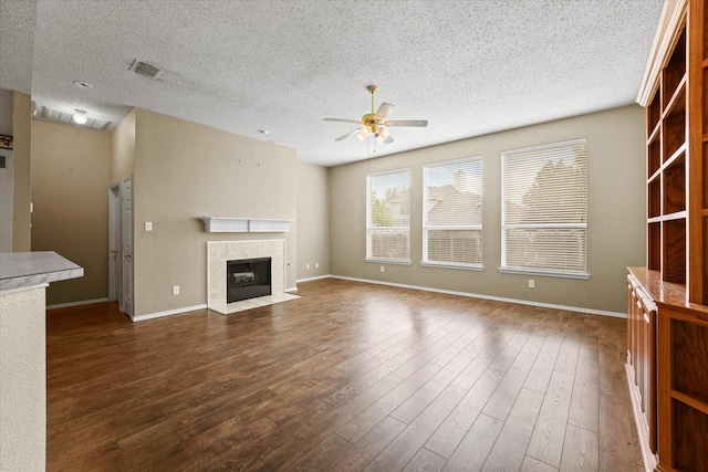 unfurnished living room featuring a textured ceiling, ceiling fan, dark hardwood / wood-style floors, and a tile fireplace