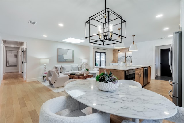 dining space featuring an inviting chandelier, a skylight, light hardwood / wood-style floors, and sink