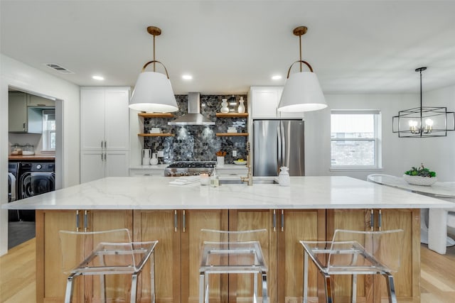 kitchen featuring decorative light fixtures, white cabinets, wall chimney exhaust hood, and stainless steel refrigerator