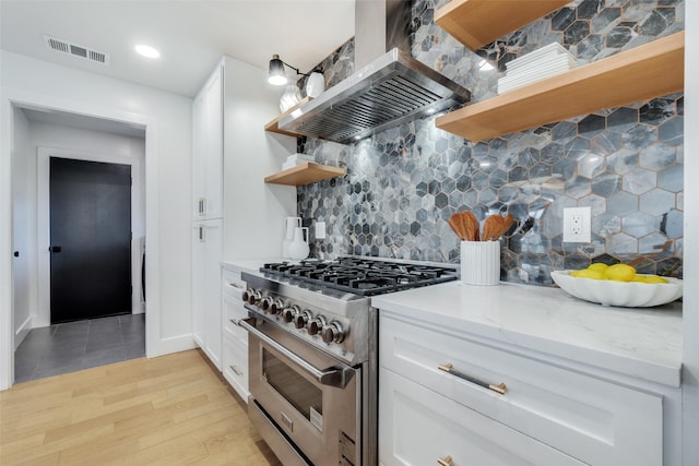 kitchen featuring backsplash, range hood, high end stove, white cabinetry, and light stone countertops