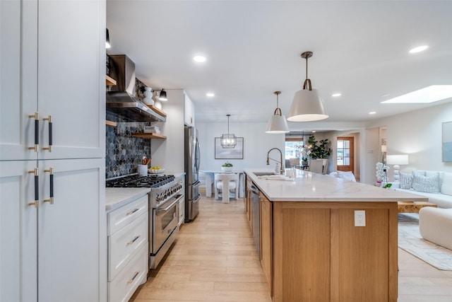 kitchen featuring wall chimney exhaust hood, white cabinetry, stainless steel appliances, sink, and a center island with sink