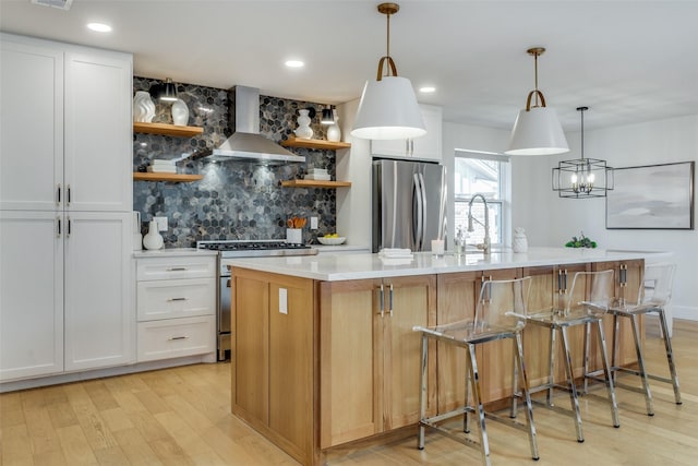 kitchen featuring an island with sink, appliances with stainless steel finishes, decorative backsplash, wall chimney range hood, and white cabinets