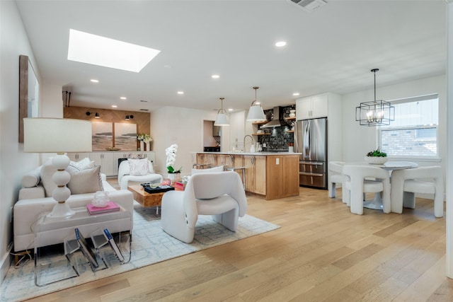 living room featuring light hardwood / wood-style floors, a skylight, and a chandelier