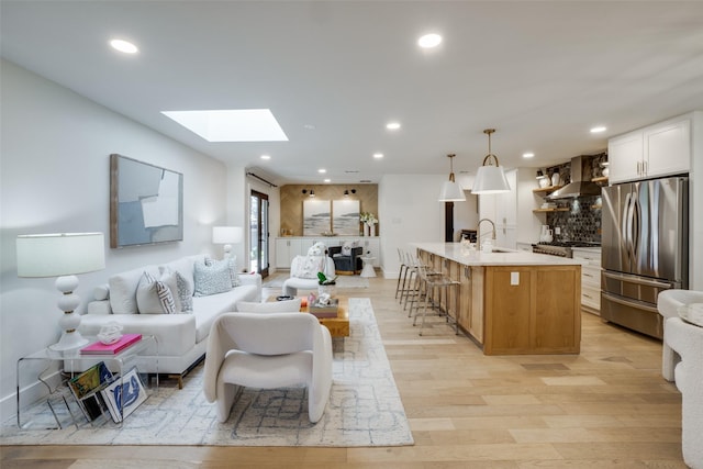 living room with sink, light hardwood / wood-style flooring, and a skylight