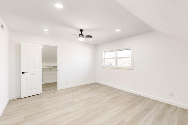 unfurnished bedroom featuring ceiling fan, lofted ceiling, light wood-type flooring, a spacious closet, and a closet