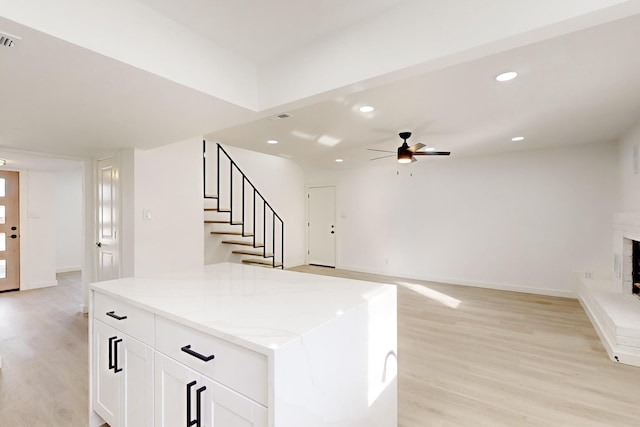 kitchen featuring ceiling fan, a fireplace, a kitchen island, light hardwood / wood-style flooring, and white cabinets