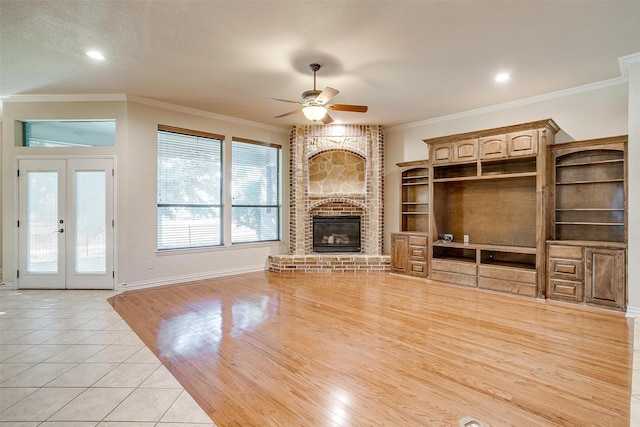 unfurnished living room with ceiling fan, a fireplace, light tile patterned flooring, ornamental molding, and french doors