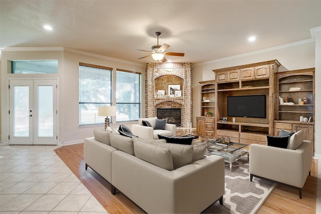 living room featuring french doors, a brick fireplace, ornamental molding, ceiling fan, and light tile patterned flooring