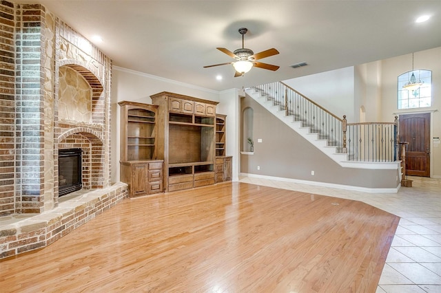 unfurnished living room with ceiling fan, light tile patterned floors, crown molding, and a fireplace