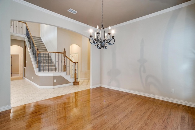 spare room featuring light hardwood / wood-style floors, crown molding, and an inviting chandelier