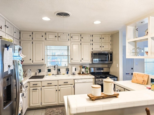 kitchen with light tile patterned floors, stainless steel appliances, decorative backsplash, tile counters, and sink