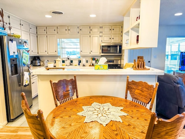 kitchen featuring light tile patterned floors, kitchen peninsula, tile counters, stainless steel appliances, and white cabinets