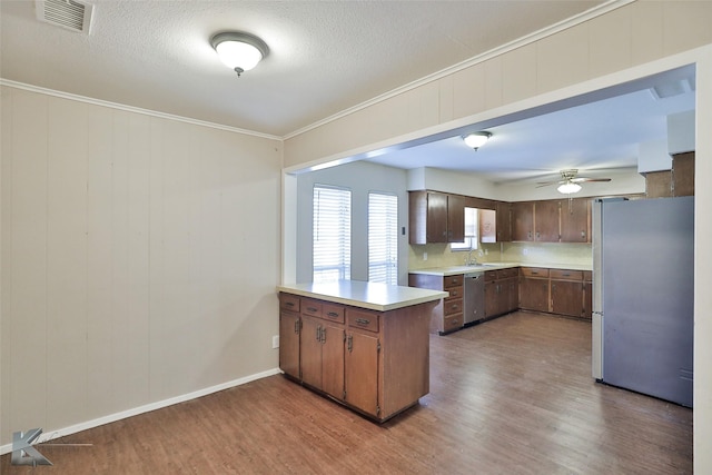 kitchen with kitchen peninsula, appliances with stainless steel finishes, ornamental molding, light hardwood / wood-style flooring, and sink