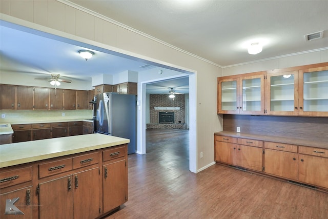 kitchen featuring hardwood / wood-style flooring, stainless steel fridge, a brick fireplace, backsplash, and ornamental molding