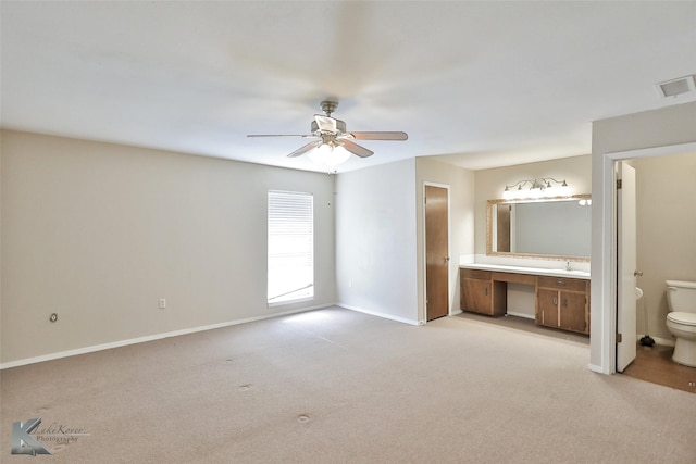 unfurnished bedroom featuring ceiling fan, light colored carpet, and ensuite bath