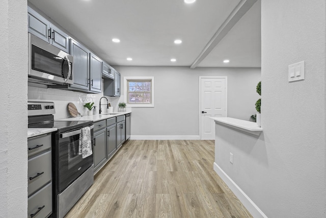 kitchen with gray cabinets, appliances with stainless steel finishes, sink, backsplash, and light hardwood / wood-style flooring