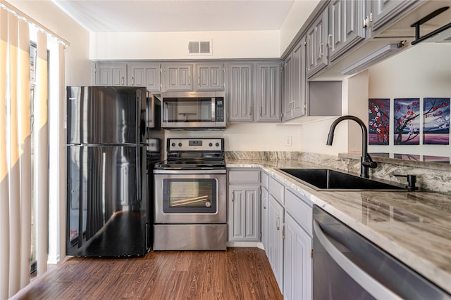 kitchen with dark hardwood / wood-style floors, gray cabinets, sink, light stone countertops, and appliances with stainless steel finishes