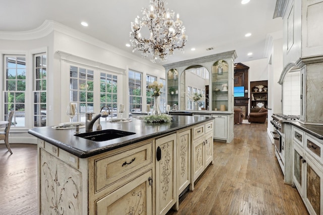 kitchen with sink, high end stainless steel range oven, hanging light fixtures, an island with sink, and a chandelier