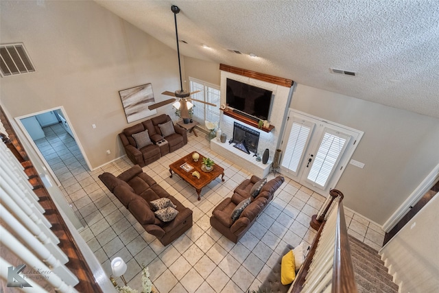 living room with a textured ceiling, ceiling fan, high vaulted ceiling, a brick fireplace, and light tile patterned floors