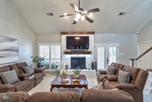 tiled living room featuring ceiling fan, vaulted ceiling, a fireplace, a textured ceiling, and french doors