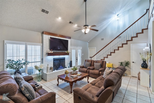 living room with a textured ceiling, ceiling fan, high vaulted ceiling, light tile patterned flooring, and a brick fireplace