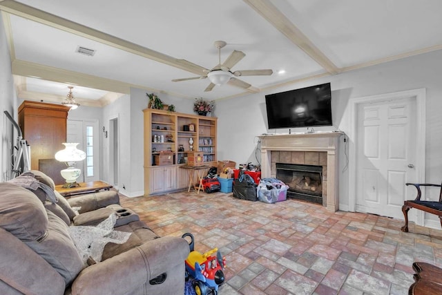 living room featuring ceiling fan, a tile fireplace, crown molding, and beamed ceiling