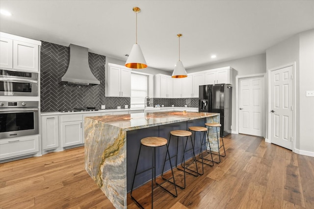 kitchen with hanging light fixtures, white cabinets, a kitchen island, and custom range hood