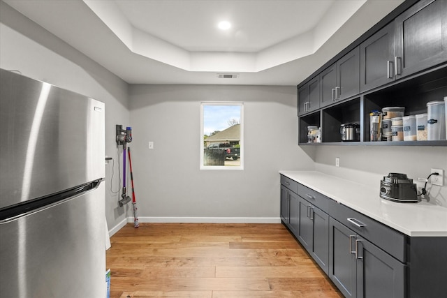 kitchen featuring stainless steel refrigerator, a tray ceiling, and light hardwood / wood-style floors