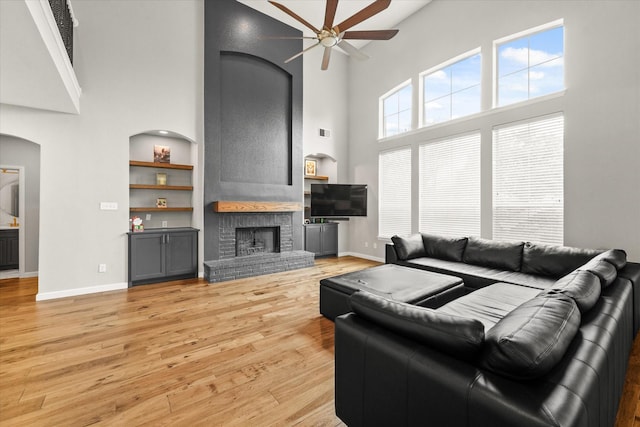 living room featuring a brick fireplace, light hardwood / wood-style flooring, a high ceiling, and ceiling fan