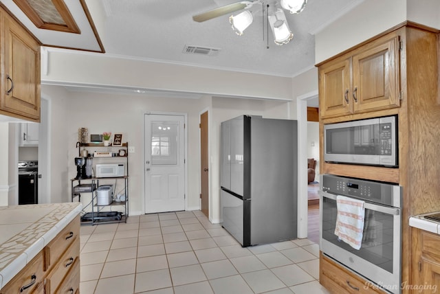 kitchen with ceiling fan, stainless steel appliances, a textured ceiling, tile counters, and light tile patterned floors