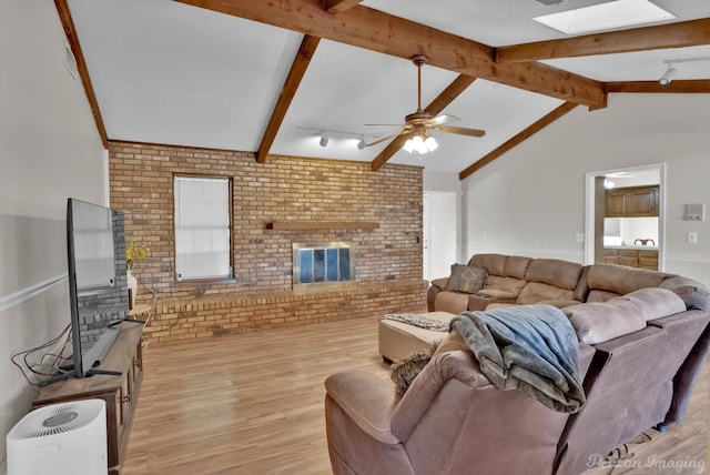 living room featuring ceiling fan, a fireplace, light hardwood / wood-style floors, lofted ceiling with beams, and brick wall