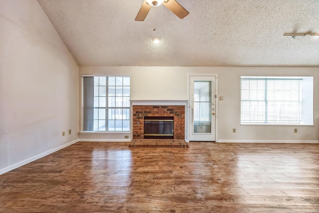 unfurnished living room with a textured ceiling, hardwood / wood-style floors, a fireplace, vaulted ceiling, and ceiling fan