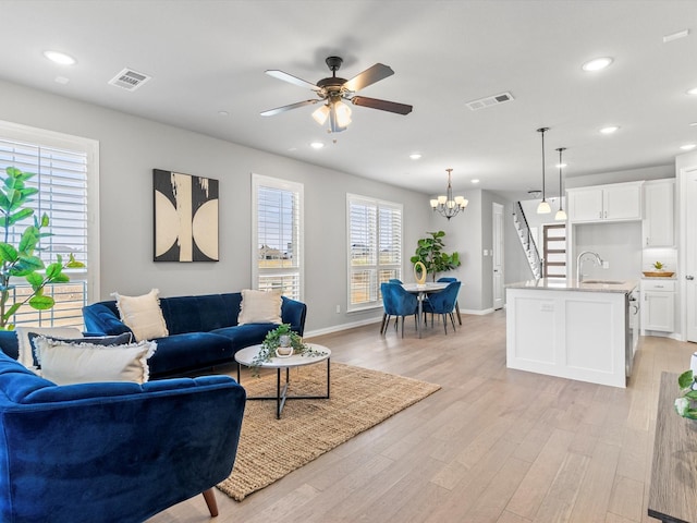 living room featuring light hardwood / wood-style floors, ceiling fan with notable chandelier, plenty of natural light, and sink