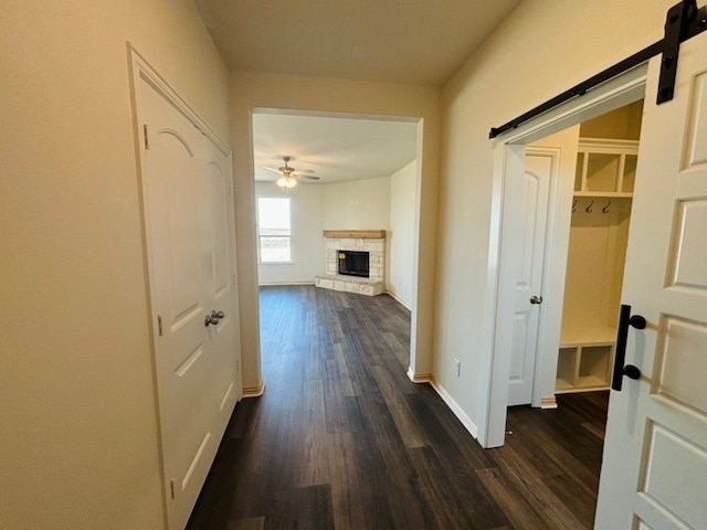 corridor with a barn door, dark wood-style floors, and baseboards